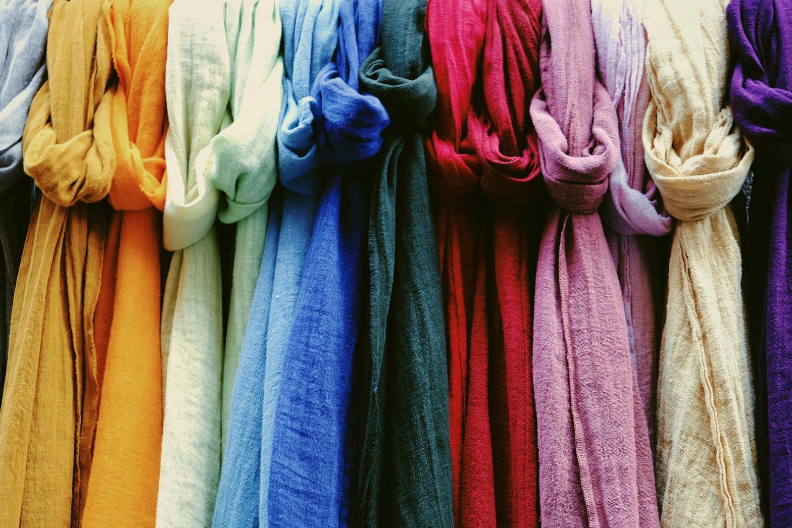 A vibrant collection of multicolored scarves displayed in a market setting.